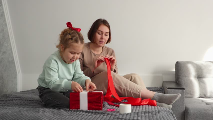 Wide shot of young mother and a little daughter pack gifts together for Valentine