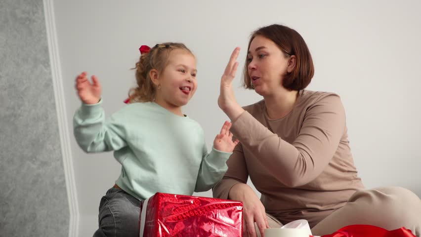 Bottom view of young mother and a little daughter pack gifts together for Valentine