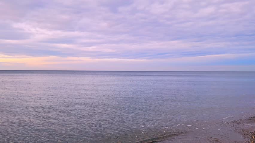 Calm seascape features gentle waves lapping against the sandy beach at dusk