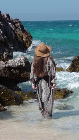 Woman standing in ocean waves near rocks, slow motion