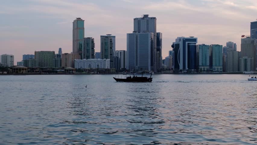 Sharjah Creek, a view of skyscrapers and the sea at sunset. A popular tourist destination in Dubai. Boats sail along the creek. Skyscrapers are caught in the rays of the setting sun.