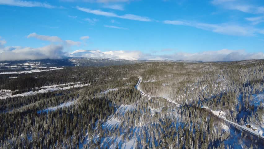 Wide aerial shot of winter mountains with a road running through the valley. Scenic travel landscape ideal for tourism and transportation concepts.
