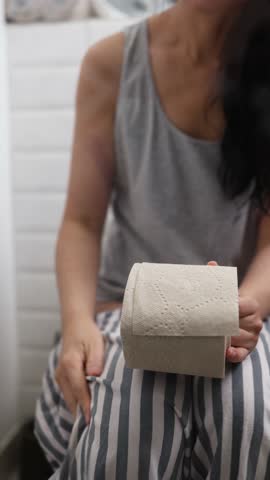 Asian woman struggling with constipation while sitting on the toilet. Vertical video.