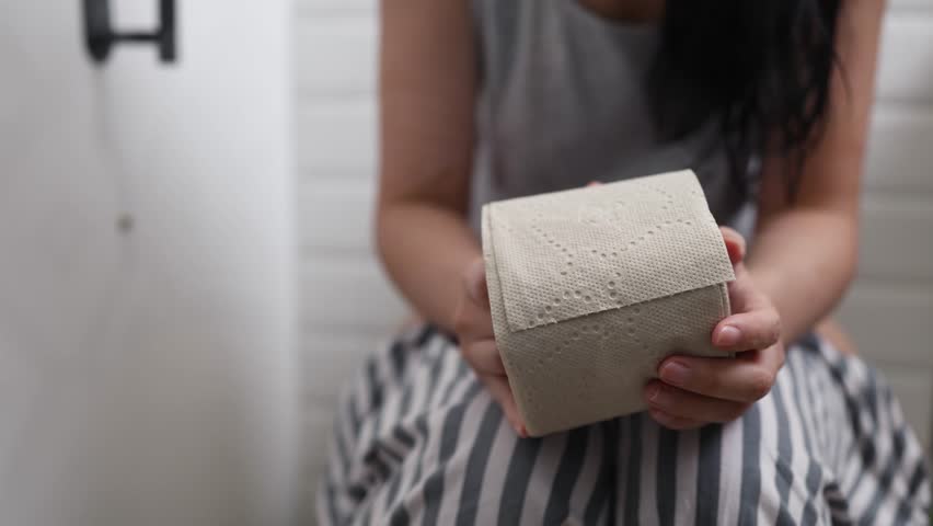Woman holding toilet paper roll while sitting on toilet bowl. digestion, constipation, Diarrhea from food poisoning, infection, abdominal, stomachache, cystitis, Insurance, Health care and Medical