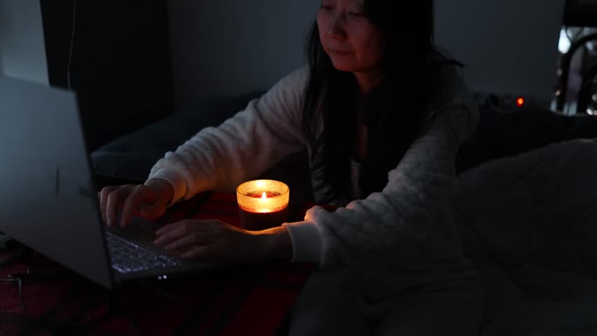 Woman working at home during an energy crisis causing blackouts. power outage, blackout, load shedding or energy crisis, concept image.