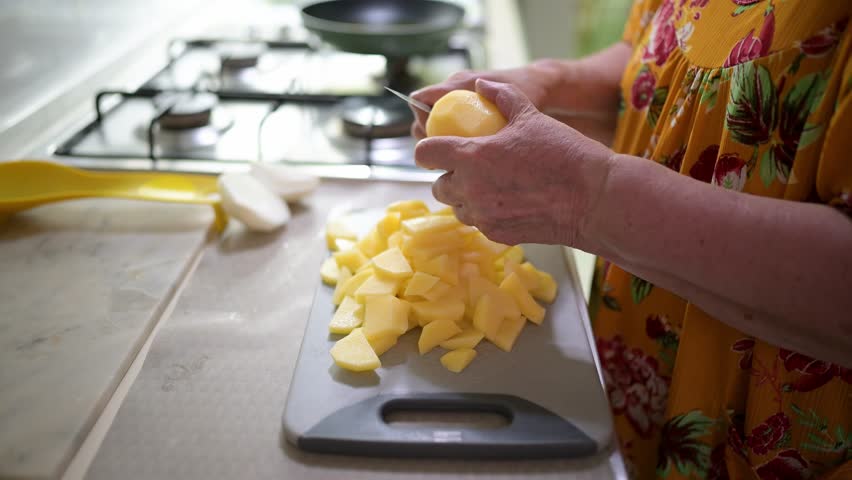 Senior woman's hands slicing raw potatoes on a cutting board
