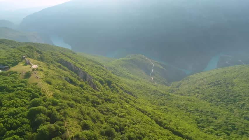 aerial footage captures the vast, green slopes and sheer cliffs of the Sulak Canyon, one of the deepest canyons in Europe. A bright turquoise river flows through the gorge under a clear sky. This natu