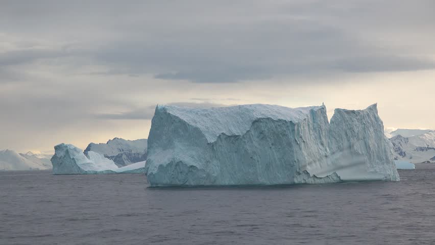 Iceberg floating in ocean under clear sky, showing large structure and blue tones in cold environment