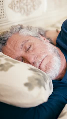 Close up of a serene senior man with gray hair and a beard sleeping soundly. Mature person resting in bed, peaceful and relaxed. Vertical