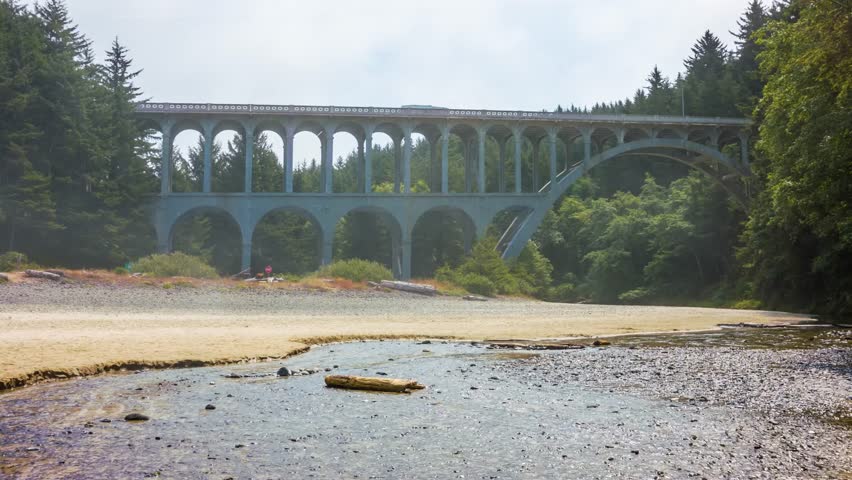 Scenic view of the historic Cape Creek Bridge on Highway 101 near Florence, Oregon. The Roman aqueduct-style arched bridge spans Cape Creek as it flows towards the Pacific Ocean, surrounded by lush co