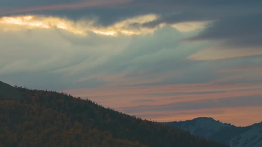 A serene and majestic landscape view of the Southern Urals mountains in Russia during a beautiful sunset or sunrise. The sky is filled with dramatic, colorful clouds in hues of orange, pink, and grey,