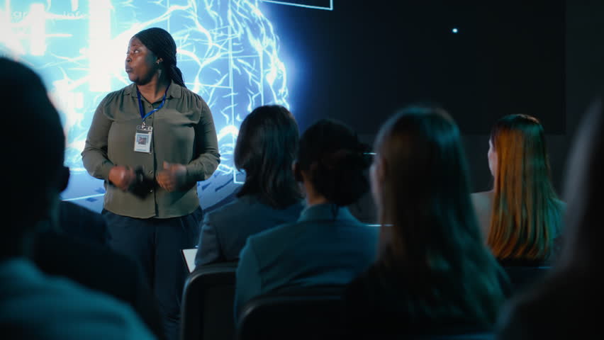 Girl in audience interacting with black female speaker presenting AI systems at business convention, showing automation and AI brain visuals for software development. Active participants. Camera B.