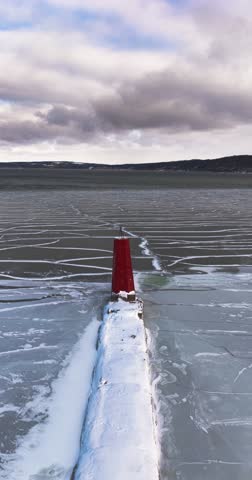 Ithaca, NY, USA - January 30, 2026 Vertical winter aerial video of the Cayuga Lake Inlet red lighthouse, beacon, with frozen water in Ithaca, NY on a sunny day with snow on the ground.