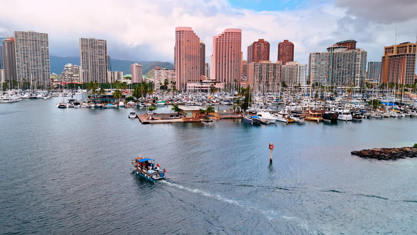 Boat goes to the shore of the Pacific Ocean in Honolulu, Hawaii, USA. Multiple yachts stand at the coast. Thick cloudscape behind the skyline at backdrop.