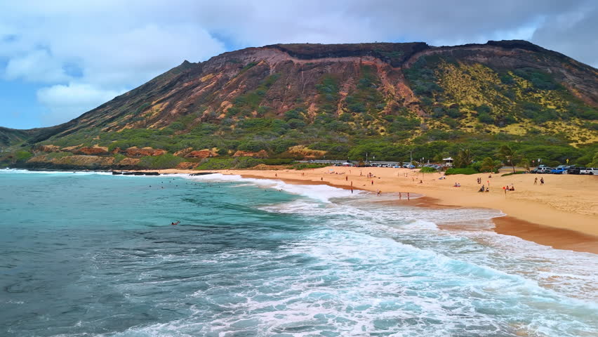 Foamy waves splash on the idyllic sandy beach. Drone footage above the Pacific Ocean at the foot of the Diamond Head Crater. Honolulu, Hawaii, Waikiki.