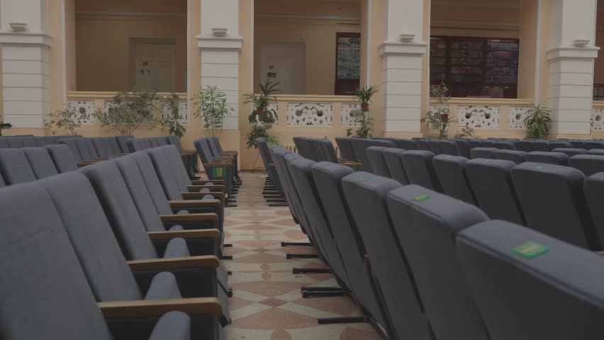 Chairs are arranged in a large hall for an upcoming event. The light from the late afternoon sun shines through the windows. The space appears empty and quiet as preparations are ongoing.