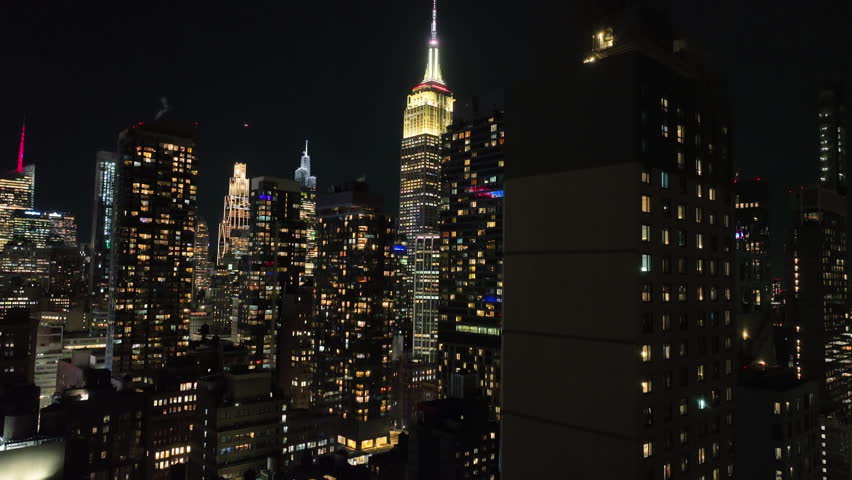Aerial view rising in middle of illuminated skyscrapers in Midtown, night in NYC