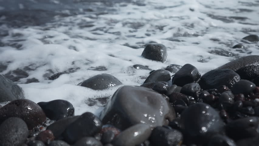 Waves wash over smooth rocks on a serene beach shoreline at low tide