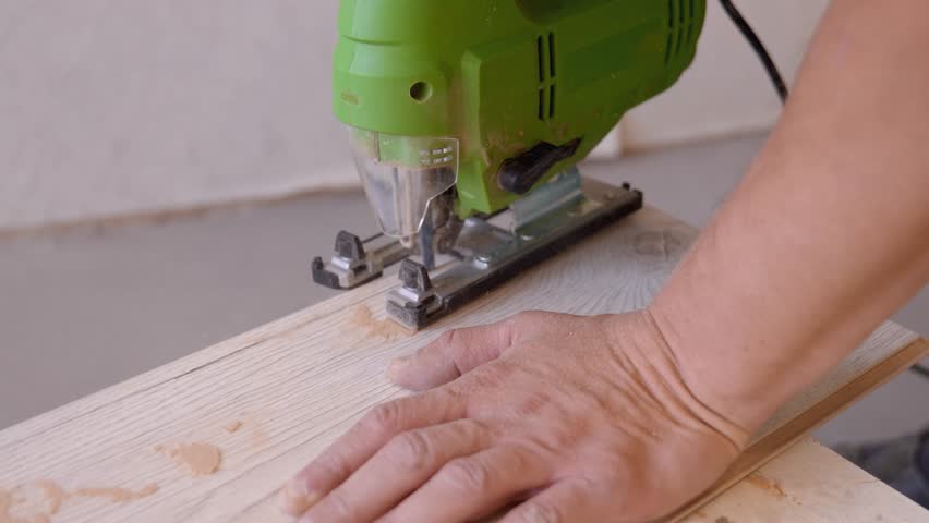 Professional worker carefully cutting a piece of laminate flooring with an electric jigsaw power tool during a home renovation, with sawdust flying from the precise blade in a workshop setting