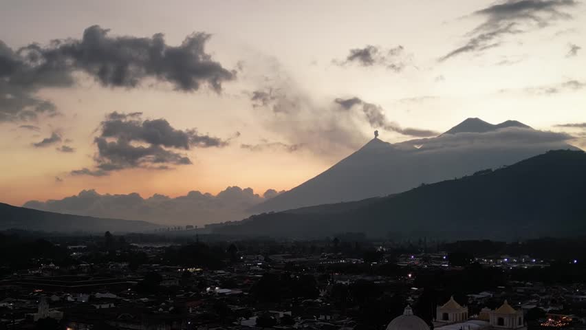 antigua guatemala sunset (scenic view of fuego acatenango volcanic eruption with cloud formation merced church agua) nightfall night time cityscape aerial drone view colorful sky volcanic highlands