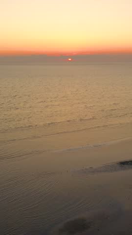 Vertical drone sunset along Nantucket shoreline, golden light on calm sea with winding sandbars and tidal pools. Tall coastal evening panorama, peaceful stock footage.