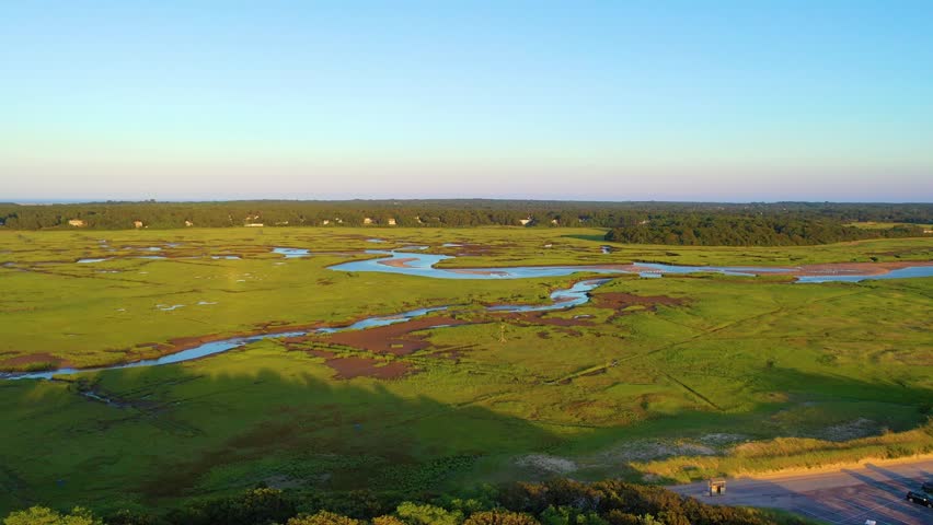 Drone aerial of coastal marshland with river-like bends and tidal creeks cutting through bright green grasses. Peaceful nature scenery, wide panorama, cinematic 4K b-roll.