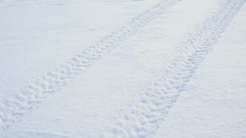 Clear fresh parallel vehicle tire tracks pressed into vast pristine white snow surface in winter