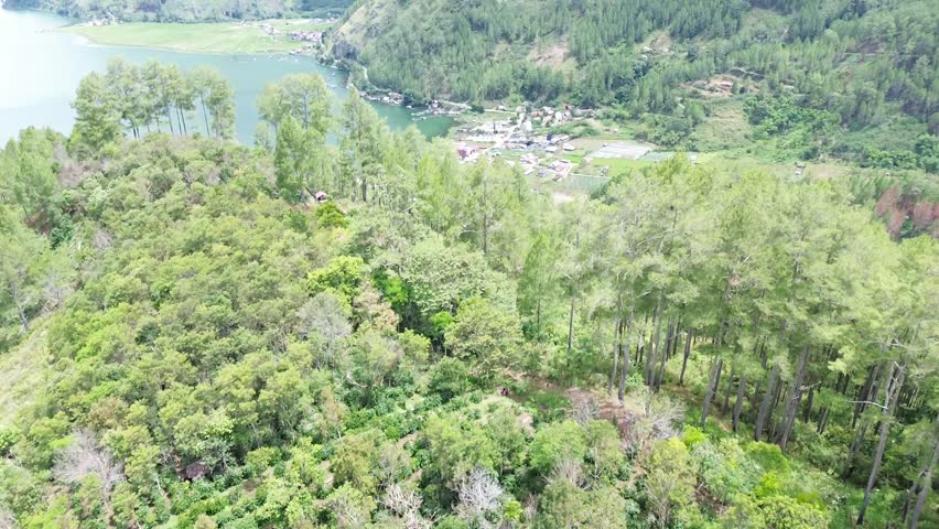 A serene lake is surrounded by lush green mountains and a small village nestled among the trees, showcasing natural beauty and tranquility in a rural setting with dense foliage and majestic landscape views, creating a picturesque and idyllic atmosphere with a mix of water, land, and sky.