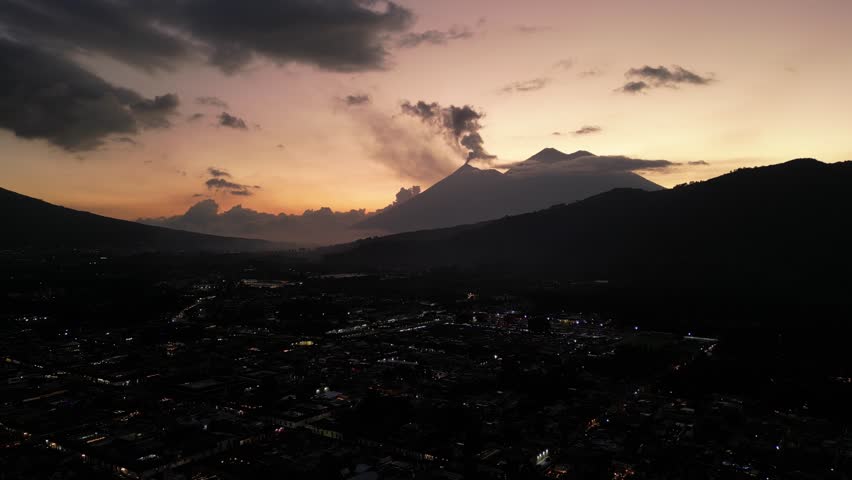 antigua guatemala sunset (scenic view of fuego acatenango volcanic eruption with cloud formation merced church agua) nightfall night time cityscape aerial drone view colorful sky volcanic highlands