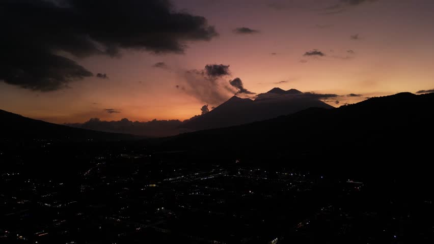 antigua guatemala sunset (scenic view of fuego acatenango volcanic eruption with cloud formation merced church agua) nightfall night time cityscape aerial drone view colorful sky volcanic highlands