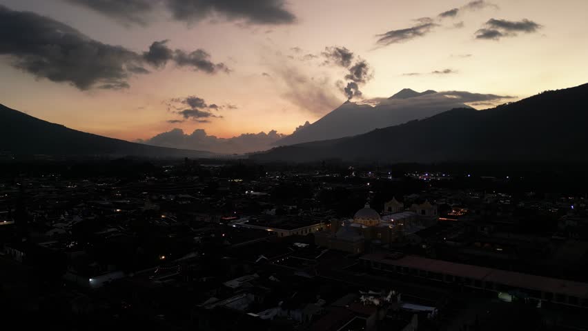 antigua guatemala sunset (scenic view of fuego acatenango volcanic eruption with cloud formation merced church agua) nightfall night time cityscape aerial drone view colorful sky volcanic highlands