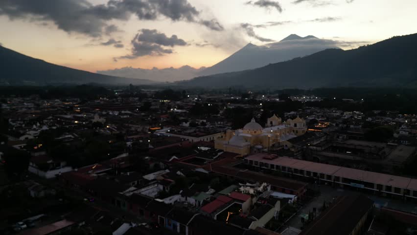 antigua guatemala sunset (scenic view of fuego acatenango volcanic eruption with cloud formation merced church agua) nightfall night time cityscape aerial drone view colorful sky volcanic highlands