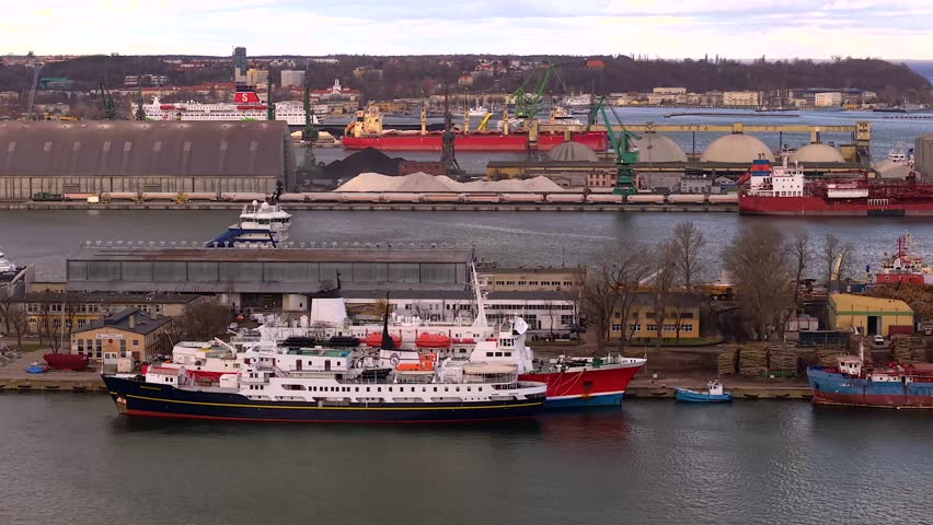 Establishing aerial shot of the port of gdynia in poland, showing various cargo ships, tankers, and cranes along the industrial waterfront