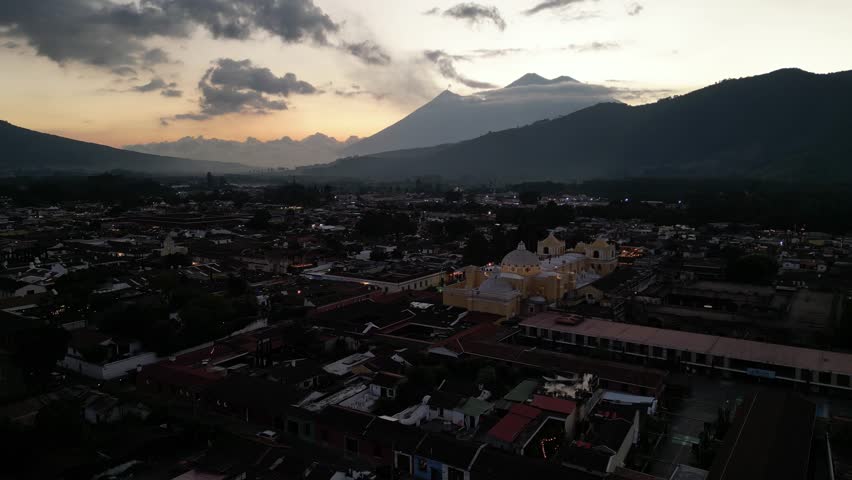 antigua guatemala sunset (scenic view of fuego acatenango volcanic eruption with cloud formation merced church agua) nightfall night time cityscape aerial drone view colorful sky volcanic highlands