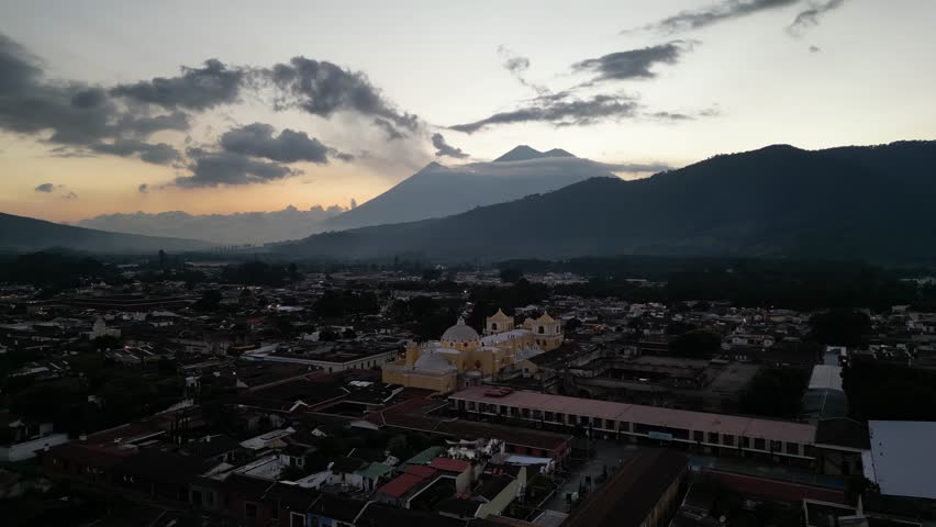 antigua guatemala sunset (scenic view of fuego acatenango volcanic eruption with cloud formation merced church agua) nightfall night time cityscape aerial drone view colorful sky volcanic highlands