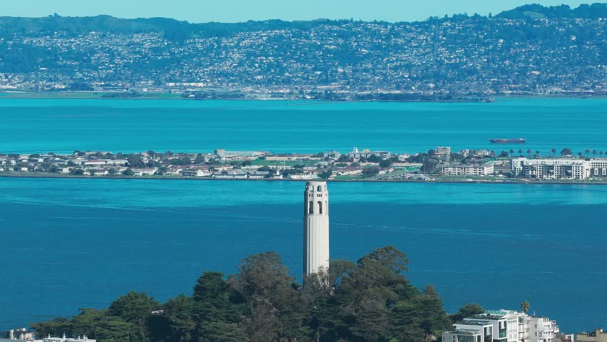 Aerial telephoto panning shot of Coit Tower with Treasure Island in the distance on a bright sunny day in San Francisco. 4K