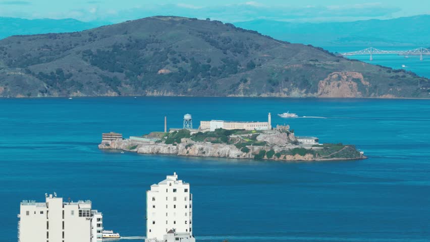 Telephoto panning aerial shot of Alcatraz Island with buildings in the foreground on a beautiful day in San Francisco, California. 4K