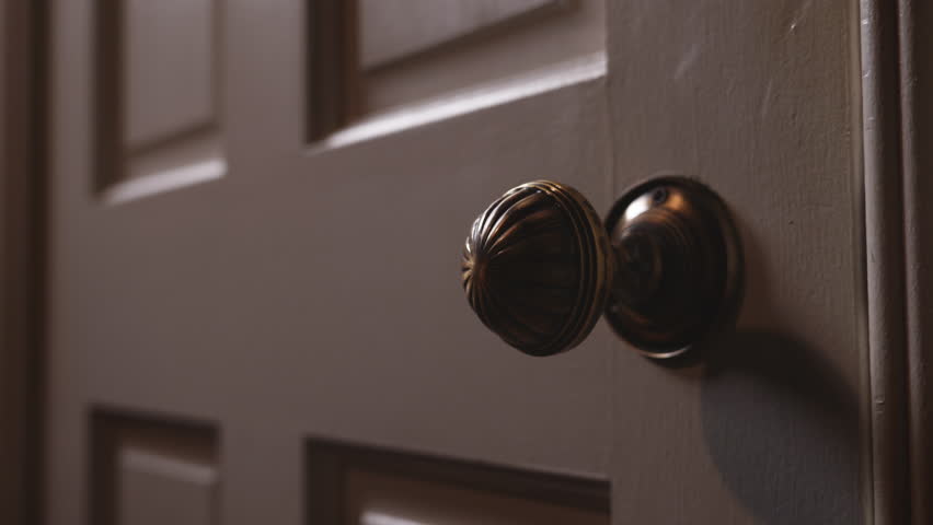 A closeup view of a door an ornate knob slowly opening, revealing darkness beyond.