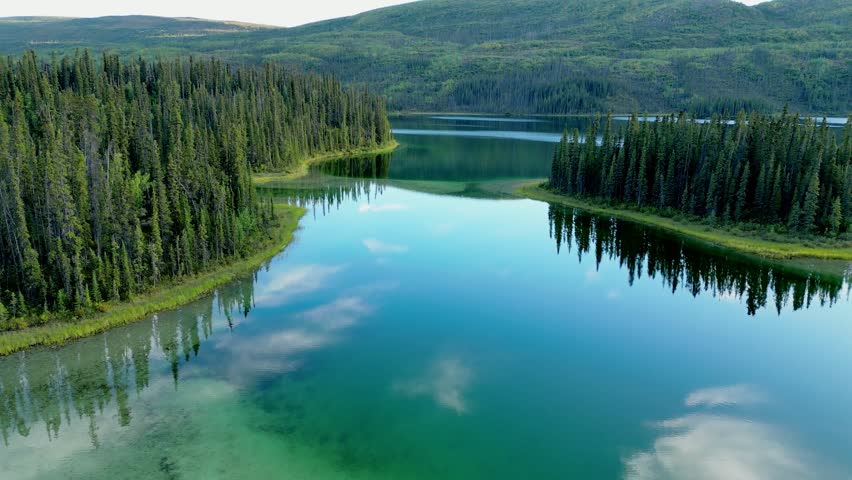 Slow drone flyover of Little Fox Lake in Yukon, Canada, showing vibrant forest, turquoise water, reflections, and a water channel between an island and peninsula.