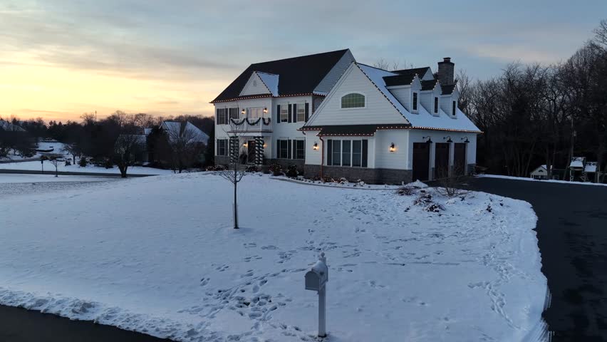 Calm winter sunset over luxury suburban home in America, showing snow-covered garden and quiet residential surroundings. Aerial shot with soft evening light in rural district of town.
