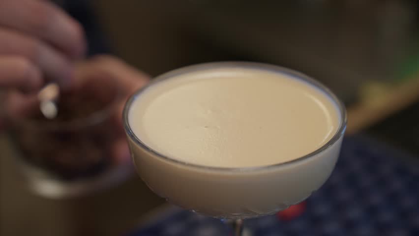 Hand placing coffee beans on foamy cocktail in coupe glass close up