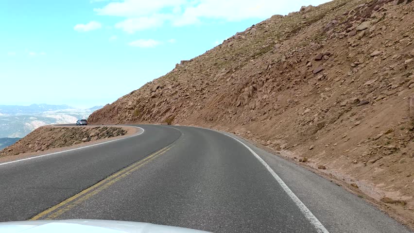 Vehicle navigating the winding Pikes Peak Highway through Colorados Rocky Mountains, offering dramatic high altitude vistas and a thrilling scenic road trip experience