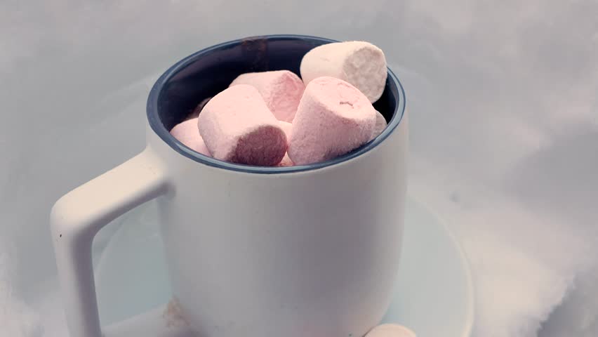 Hot chocolate and marshmallows in a big ceramic mug on a saucer against a snowy backdrop, winter composition.