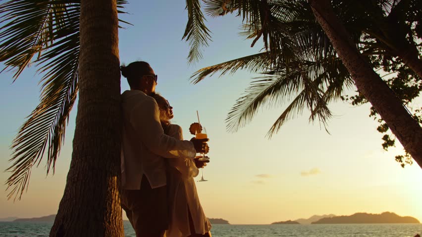 The man hugs a woman. Cute loving couple in white shirt and sunglasses, near palm tree, kissing, hugging, relax and drinking cocktail. Concept tropical summer vacations, relationship wedding love
