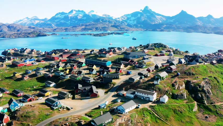Picturesque Greenland landscape featuring small boats along the coast, colorful houses, snow-covered mountains, winding roads, rocky terrain, and calm sea water. Peaceful Arctic scenery showcasing remote coastal life, natural beauty, and dramatic northern environment in high resolution.