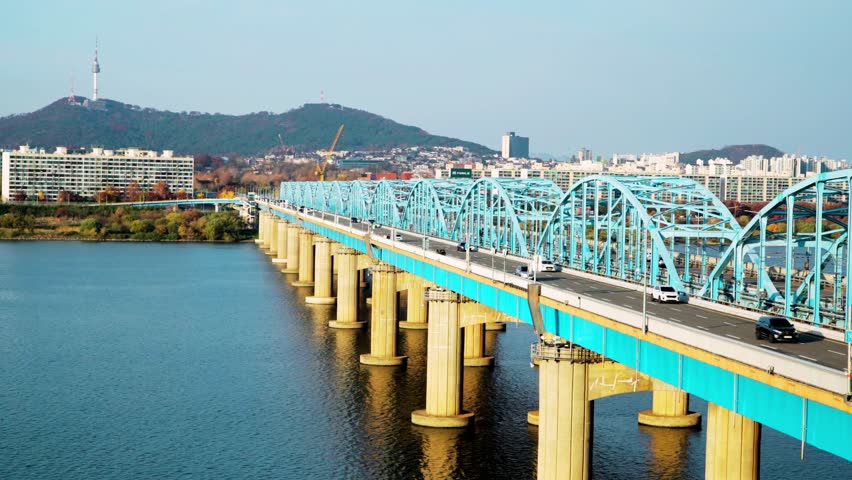 Static view of car traffic on Dongjak Bridge over the Han River in Seoul, South Korea, with N Seoul Tower visible in the background. Evening cityscape showcasing urban infrastructure, flowing vehicles, illuminated skyline, and modern metropolitan atmosphere, high-resolution, cinematic perspective.