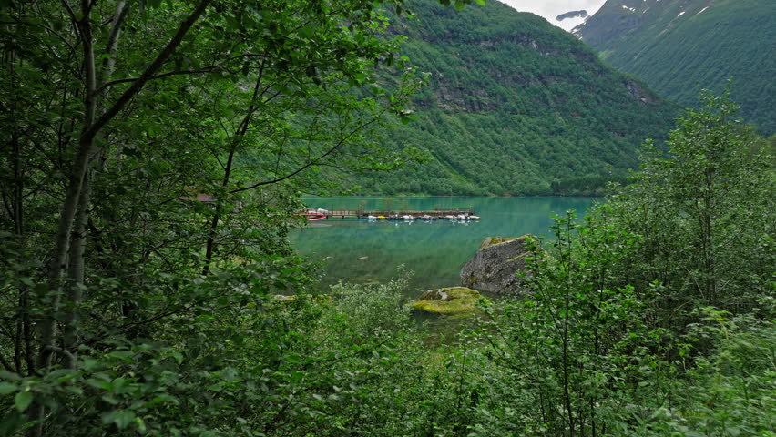 Lovatnet Lake shoreline in Loen Valley, Norway. Turquoise water, mossy rocks and green mountains create a peaceful summer lakeside mood.