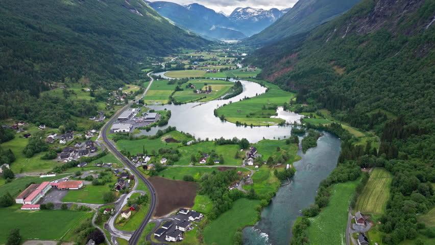 Wide drone panorama of Stryn landscape and river bends. Calm, scenic view of rural Norway with fields, houses, and flowing water framed by steep forested slopes.