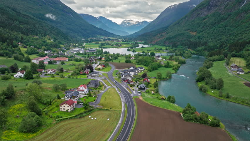 Aerial view of Stryn valley with river bends, farmland, and scattered houses in western Norway. Calm summer drone footage shows rural landscape framed by forested mountains.