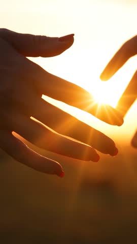Close-up of the silhouettes of a couple in love holding their hands together and the golden sun gently setting below the horizon. The man and woman have their hands clasped tightly, romantic scene at sunset, slow motion. Couple stands close together deep bond and emotional connection.